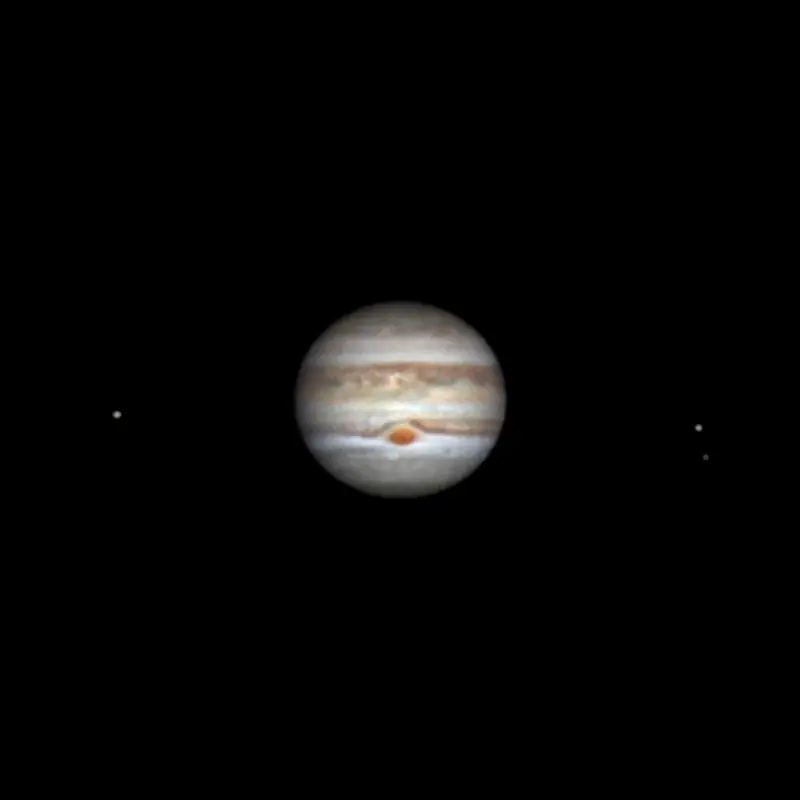 Jupiter raidallisena kiekkona ja sen vieressä kaksi pientä kuuta pisteinä.