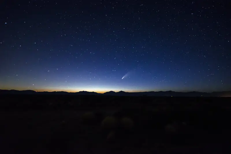 Komeetta NEOWISE pyrstöineen matalalla aamuhämärässä vuorten yllä.