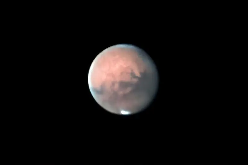 Mars oranssina kiekkona, jossa näkyy tummia alueita ja valkoinen napalakki.